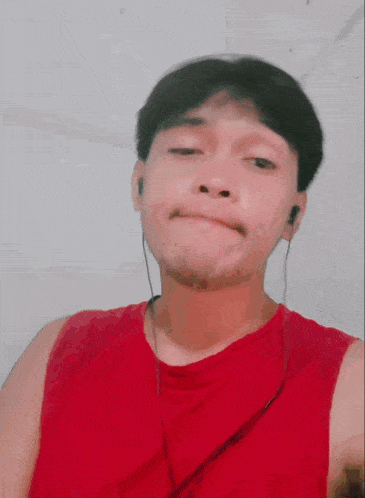a man wearing a red tank top and ear buds is making a funny face