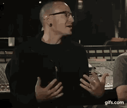 a man with glasses and a ring on his finger is talking to someone in a recording studio .