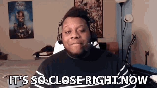 a man wearing headphones and a black shirt says it 's so close right now