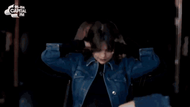 a woman in a denim jacket is standing in a dark room .