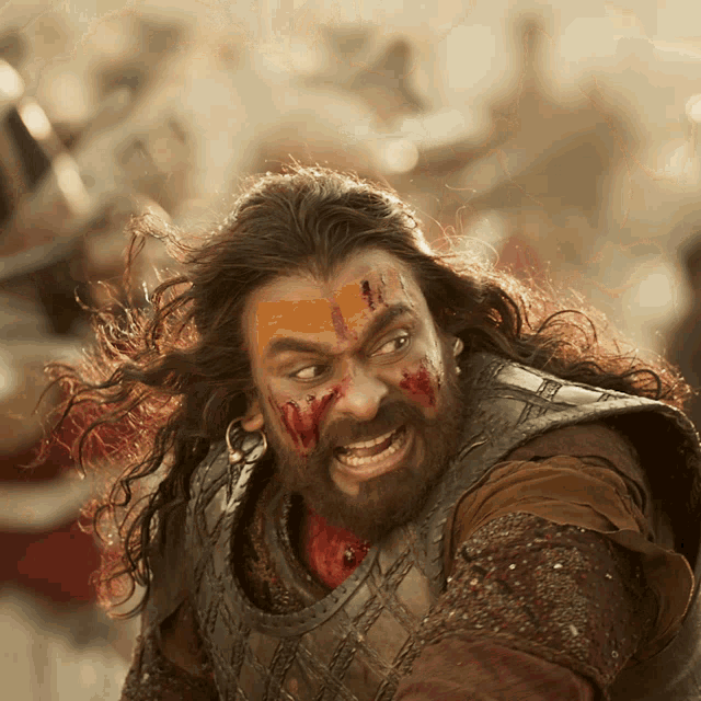 a man with long hair and a beard has blood on his face and is wearing armor