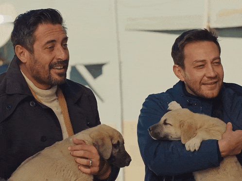 a man in a blue jacket is holding a puppy in his arms