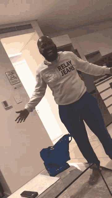 a man wearing a relay jeans sweatshirt is standing in a room with his arms outstretched