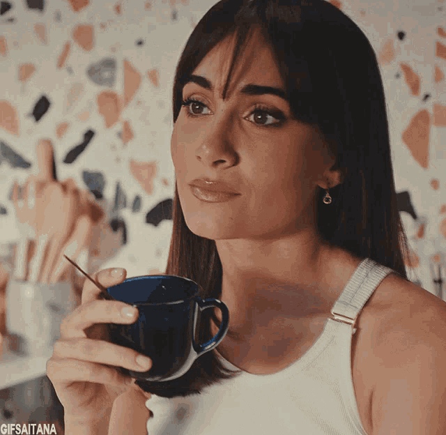 a woman in a white tank top is drinking from a blue cup with a spoon