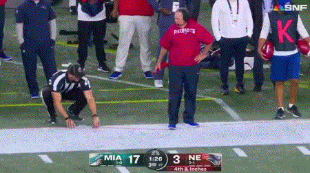 a man in a red patriots shirt is kneeling on the field