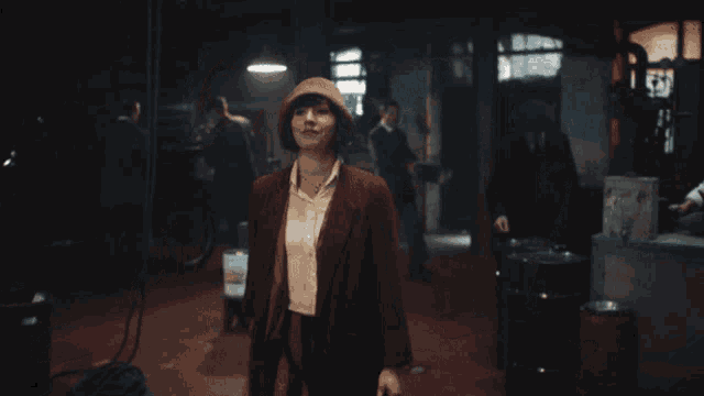 a woman in a brown coat and hat stands in a room