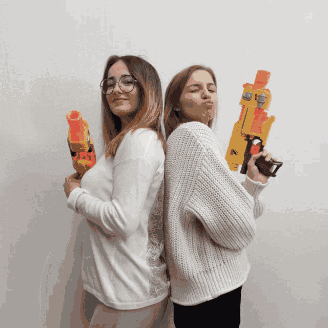 two girls standing back to back holding nerf guns and making funny faces