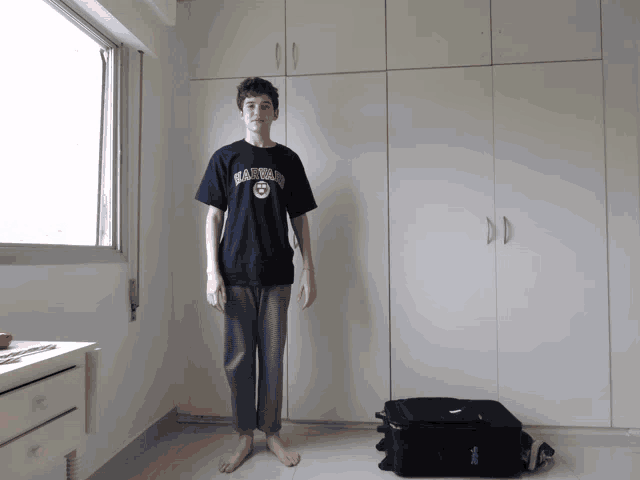 a young man wearing a shirt that says harvard is standing in a room