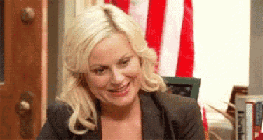 a woman in a suit is smiling in front of an american flag .
