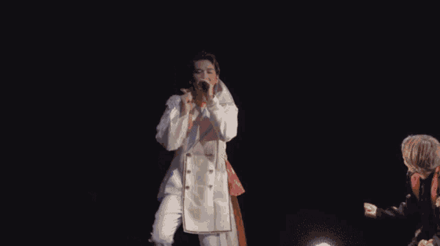 a man in a white robe is singing into a microphone in the dark