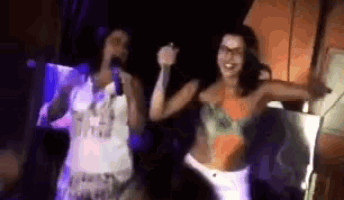 two women are singing into microphones while dancing in a dark room