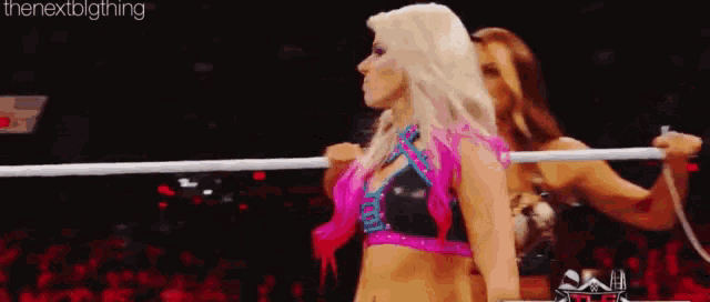 two female wrestlers are standing in a ring holding a rope .