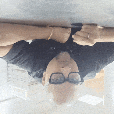 a man wearing glasses and a black shirt is upside down on a table