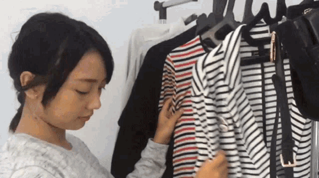 a woman is looking at a striped shirt in a closet