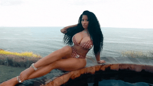 a woman in a bikini sits on a wooden ledge overlooking a body of water