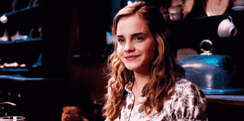 a young woman is smiling while sitting at a table in a kitchen .