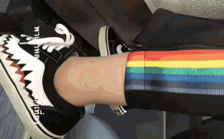 a person wearing a pair of rainbow striped socks and a pair of black and white shoes