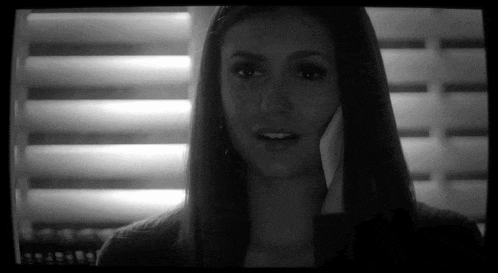 a black and white photo of a woman talking on a cell phone in front of a window .