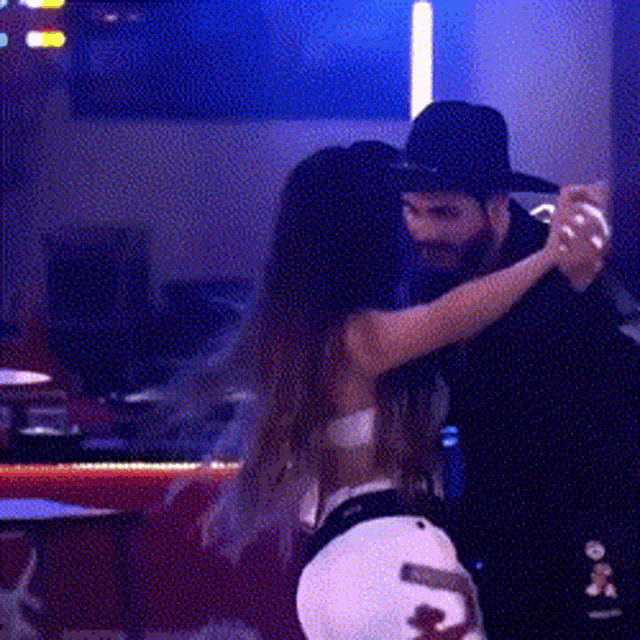 a man and a woman are dancing in a dark room and the woman is wearing a white hat with the letter o on it