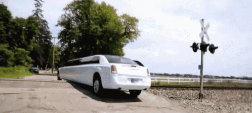 a white limousine is driving down a road near a railroad crossing