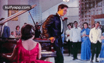 a woman in a red dress is playing a piano while a man in a tuxedo is dancing .