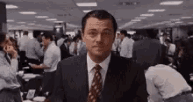 a man in a suit and tie is standing in front of a crowd of people in a room .