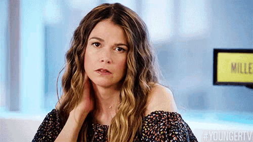 a woman with long wavy hair is sitting on a couch with her hands on her neck .