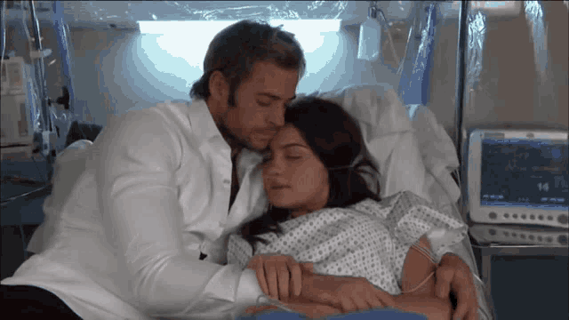 a man and a woman are laying in a hospital bed with a monitor that says 14 on it