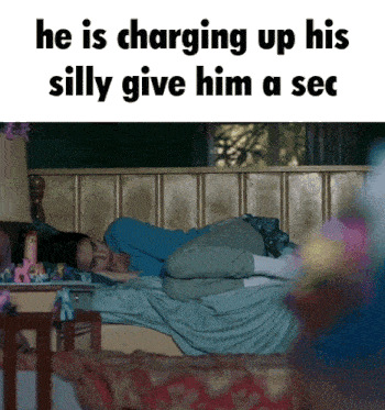 a woman is laying on a bed with a caption that says he is charging up his silly give him a sec