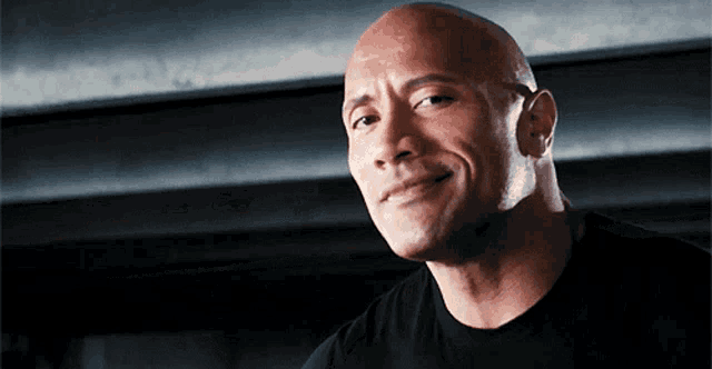 a bald man wearing a black shirt is smiling and looking at the camera