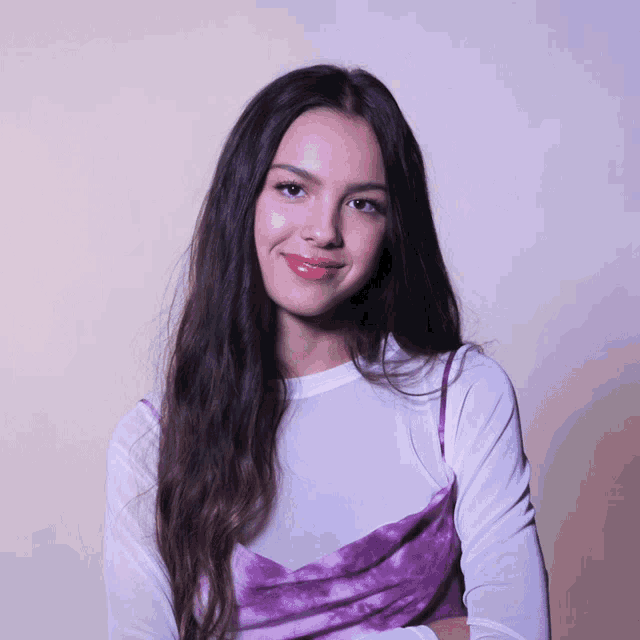 a girl with long dark hair wearing a white shirt and a purple dress