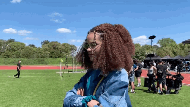 a woman with curly hair wearing sunglasses stands on a field