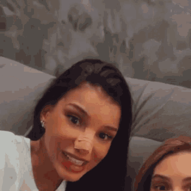 two women are sitting on a couch and smiling at the camera .