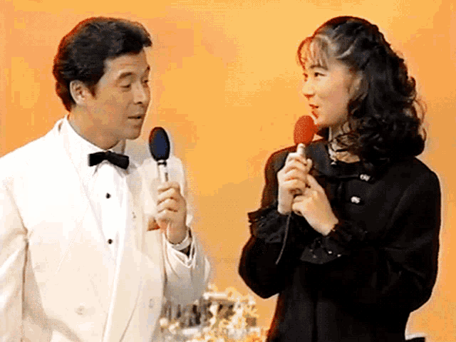 a man in a tuxedo is holding a microphone next to a woman