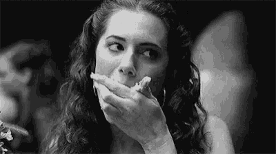 a woman is eating a piece of bread with her hand over her mouth in a black and white photo .