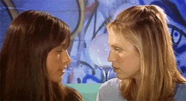 two women are looking at each other in front of a graffiti wall ..