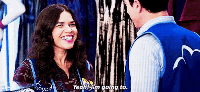 a woman in a plaid shirt is smiling while talking to a man in a blue vest with a bird on it .