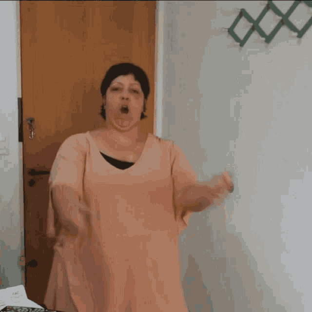 a woman in a pink dress is standing in front of a door with her mouth open