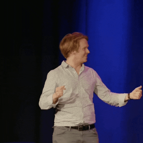 a man in a white shirt is dancing in front of a blue wall