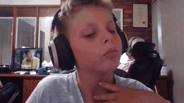 a boy wearing headphones looks at the camera with a certificate hanging on the wall behind him