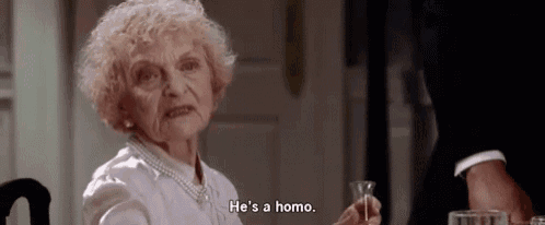 an elderly woman is sitting at a table holding a glass of wine and saying `` he 's a homo '' .