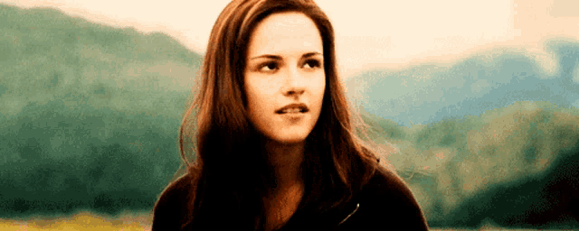 a woman with long brown hair is standing in front of mountains .