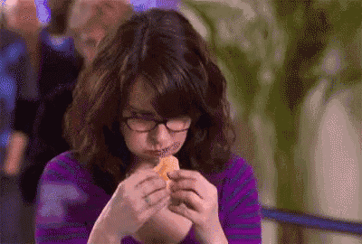 a woman wearing glasses is eating a piece of food in a purple shirt .