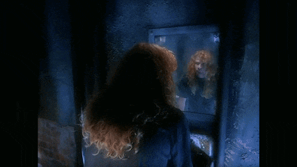 a man with long red hair is looking at himself in a mirror