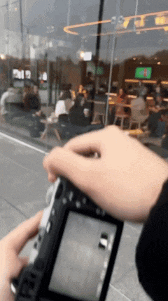 a person is holding a camera in front of a window with a reflection of a restaurant