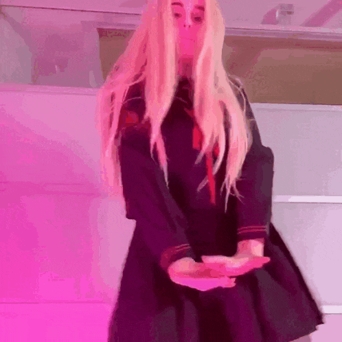 a blonde girl in a black dress is dancing in front of a pink background .