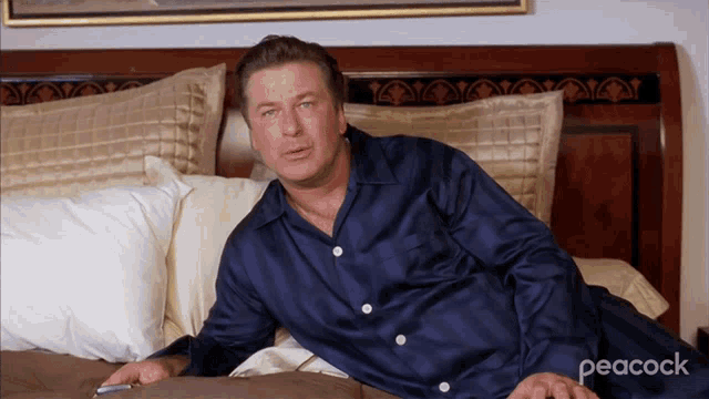 a man in a blue shirt is laying on a bed with peacock written in the corner