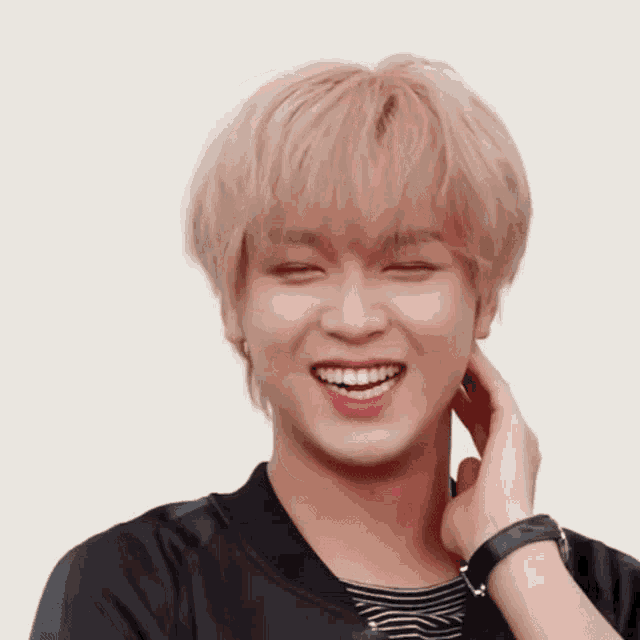 a young man with blonde hair is smiling with his eyes closed and his hand on his face .