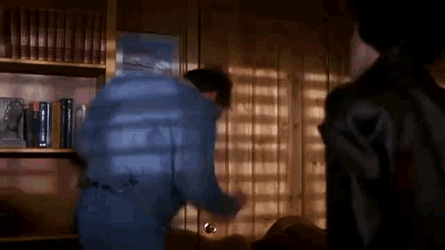 a man in a blue shirt is opening a door in a room with bookshelves .