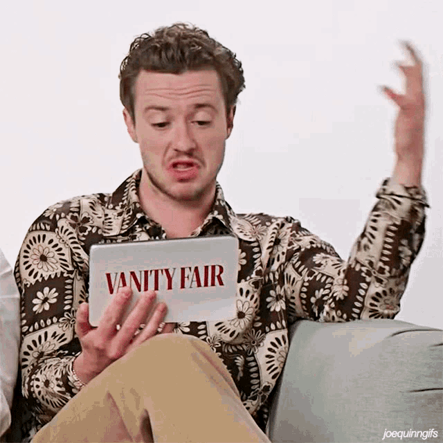 a man is sitting on a couch holding a vanity fair sign